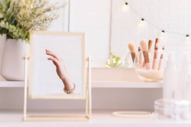 İnci bilezikler takmış bir kadının masa aynasında yansıması. Noel, ampuller, okaliptüs, köknar makyaj malzemeleriyle makyaj masasındaki vazoda çam dalları. Dikey