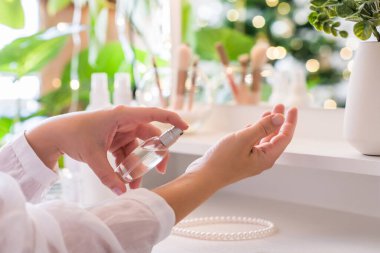 Makyaj aksesuarları ve masa aynasıyla eline parfüm süren bir kadın. Kişisel Bakım. 