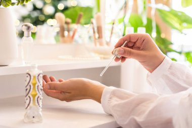 Makyaj aksesuarları ve masa aynasıyla eline parfüm süren bir kadın. Noel, ampuller, okaliptüs, köknar, bir vazoda çam dalları.