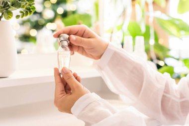 Makyaj aksesuarları ve masa aynasıyla eline parfüm süren bir kadın. Noel, ampuller, okaliptüs, köknar, bir vazoda çam dalları.