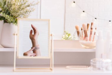 Masadaki aynada yansıyan inci bilezikli kadın makyaj aksesuarlarıyla makyaj masasında. Kişisel Bakım. 