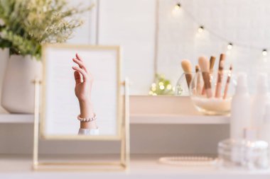 İnci bilezikler takmış bir kadının masa aynasında yansıması. Noel, ampuller, okaliptüs, köknar makyaj malzemeleriyle makyaj masasındaki vazoda çam dalları. Dikey