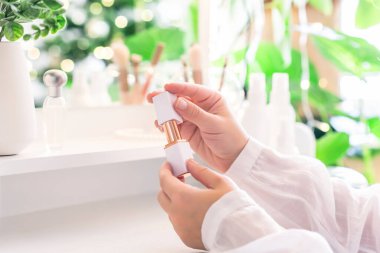 Makyaj malzemeleriyle makyaj masasının yanında oturan bir kadın. Noel ağacının yansıması, masa aynasında ampuller..