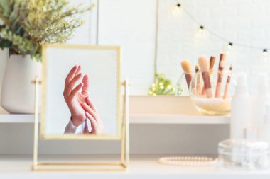 Kadın elinin masa aynasında yansıması. Noel, ampuller, okaliptüs, köknar, makyaj malzemeleriyle makyaj masasındaki vazoda çam dalları..