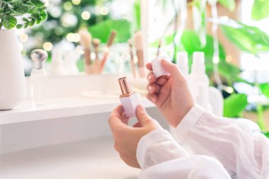 Makyaj aksesuarları ve masa aynasıyla makyaj masasının yanında oturan bir kadın. Beyaz iç mekan