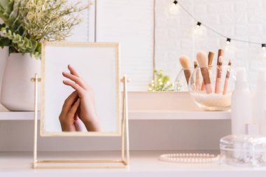 Kadın elinin masa aynasında yansıması. Noel, ampuller, okaliptüs, köknar, makyaj malzemeleriyle makyaj masasındaki vazoda çam dalları..