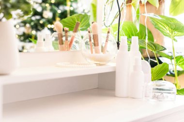 Makyaj aksesuarları ve masa aynasıyla eline parfüm süren bir kadın. Noel, ampuller, okaliptüs, köknar, bir vazoda çam dalları.