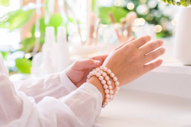 Kadın takı takıyor, eline inci bilezikler takıyor makyaj malzemeleriyle makyaj masasının yanında oturuyor..