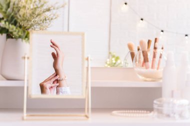 Masadaki aynada yansıyan inci bilezikli kadın makyaj aksesuarlarıyla makyaj masasında. Kişisel bakım. Beyaz iç mekan