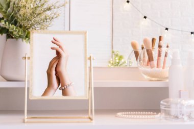 İnci bilezikler takmış bir kadının masa aynasında yansıması. Noel, ampuller, okaliptüs, köknar makyaj malzemeleriyle makyaj masasındaki vazoda çam dalları. Dikey