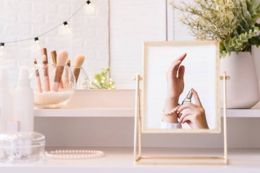 Masa aynasındaki kadın parfümünü eline sürerken yansıması. Kadın parti hazırlığı. Noel, ampuller, okaliptüs, köknar, makyaj malzemeleriyle makyaj masasındaki vazoda çam dalları.. 