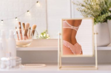 İç çamaşırlı kadın vücudunun masa aynasında yansıması. Kadın parti hazırlığı. Noel, ampuller, okaliptüs, köknar, makyaj malzemeleriyle makyaj masasındaki vazoda çam dalları.. 