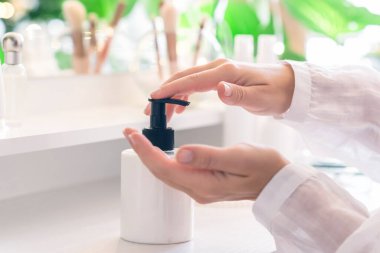 Kadın eline günlük krem sürüyor makyaj malzemeleri ve masa aynasıyla makyaj masasının yanında oturuyor.. 