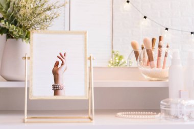 Masadaki aynada yansıyan inci bilezikli kadın makyaj aksesuarlarıyla makyaj masasında. Kişisel Bakım. 