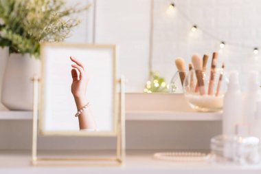 Noel, ampuller, okaliptüs, köknar makyaj malzemeleriyle makyaj masasındaki vazoda çam dalları. İnci bilezikler takmış bir kadının masa aynasında yansıması.