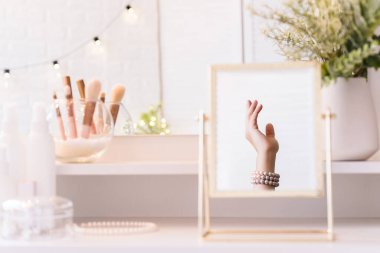 İnci bilezikler takmış bir kadının masa aynasında yansıması. Noel, ampuller, okaliptüs, köknar makyaj malzemeleriyle makyaj masasındaki vazoda çam dalları. Dikey