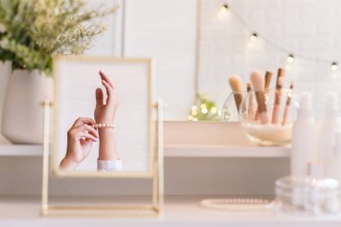 Masadaki aynada yansıyan inci bilezikli kadın makyaj aksesuarlarıyla makyaj masasında. Kişisel bakım. Beyaz iç mekan