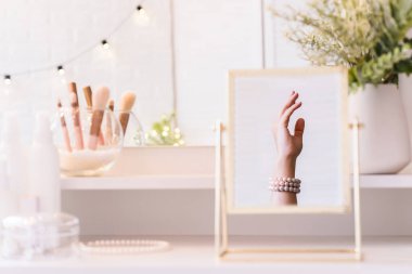 Noel, ampuller, okaliptüs, köknar makyaj malzemeleriyle makyaj masasındaki vazoda çam dalları. İnci bilezikler takmış bir kadının masa aynasında yansıması.