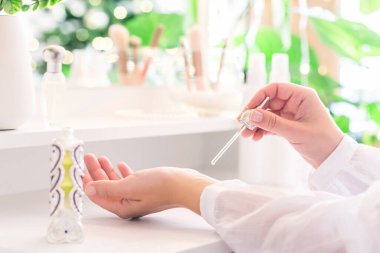 Makyaj aksesuarları ve masa aynasıyla eline parfüm süren bir kadın. Kişisel Bakım. 