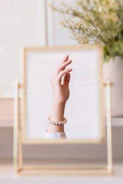 İnci bilezikler takmış bir kadının masa aynasında yansıması. Noel, ampuller, okaliptüs, köknar makyaj malzemeleriyle makyaj masasındaki vazoda çam dalları. Dikey