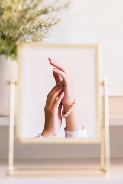 Noel, ampuller, okaliptüs, köknar makyaj malzemeleriyle makyaj masasındaki vazoda çam dalları. İnci bilezikler takmış bir kadının masa aynasında yansıması.