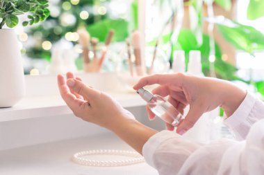 Makyaj aksesuarları ve masa aynasıyla eline parfüm süren bir kadın. Kişisel Bakım. 