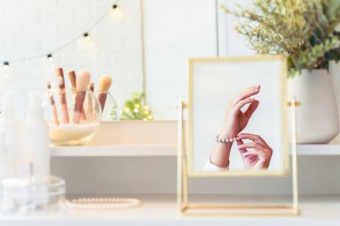 Masadaki aynada yansıyan inci bilezikli kadın makyaj aksesuarlarıyla makyaj masasında. Kişisel Bakım. 