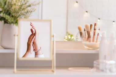 Noel, ampuller, okaliptüs, köknar makyaj malzemeleriyle makyaj masasındaki vazoda çam dalları. İnci bilezikler takmış bir kadının masa aynasında yansıması.