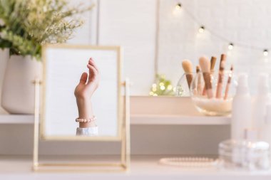 Masadaki aynada yansıyan inci bilezikli kadın makyaj aksesuarlarıyla makyaj masasında. Kişisel Bakım. 