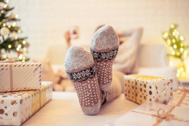 Noel ağacının yanındaki koltukta oturan kadın. Dişi bacaklar, kışın yün çoraplar, masaya koymak ve el yapımı hediye kutuları paketledikten sonra dinlenmek. Aile için hediyeler.