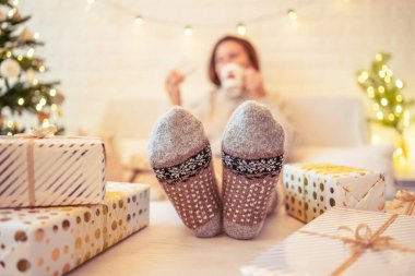 Odaklanamayan, bulanık bir kadın Noel ağacının yanında oturuyor ve aile için hediye paketlerini bitirdikten sonra bir fincan kakao ve şekerlemeyle rahatlıyor..