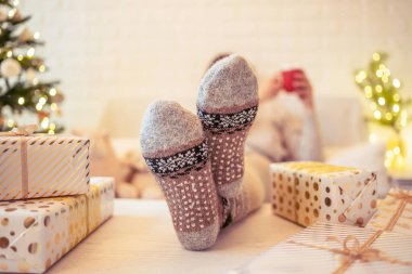 Noel ağacının yanındaki koltukta oturan kadın. Dişi bacaklar, kışın yün çoraplar, masaya koymak ve el yapımı hediye kutuları paketledikten sonra dinlenmek. Aile için hediyeler.