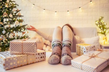 Noel ağacının yanındaki koltukta oturan kadın. Dişi bacaklar, kışın yün çoraplar, masaya koymak ve el yapımı hediye kutuları paketledikten sonra dinlenmek. Aile için hediyeler.