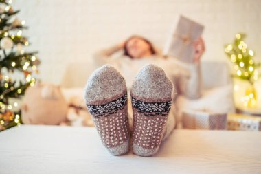 Noel ağacının yanındaki koltukta oturan kadın. Dişi bacaklar, kışın yün çoraplar, masaya koymak ve el yapımı hediye kutuları paketledikten sonra dinlenmek. Aile için hediyeler.