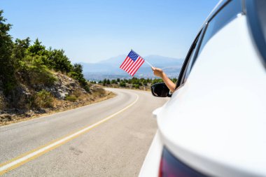 Kadın, açık arabanın camından Amerikan bayrağını tutuyor dağlarda serpentin yol boyunca sürüyor. Kavram