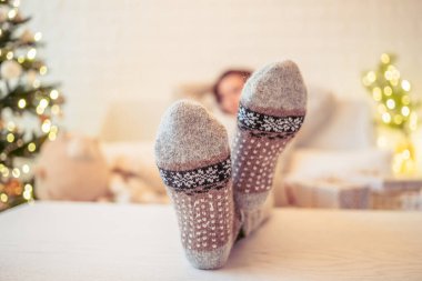 Noel ağacının yanındaki koltukta oturan kadın. Dişi bacaklar, kışın yün çoraplar, masaya koymak ve el yapımı hediye kutuları paketledikten sonra dinlenmek. Aile için hediyeler.