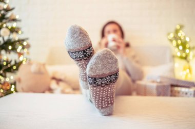 Noel ağacının yanındaki koltukta oturan kadın. Dişi bacaklar, kışın yün çoraplar, masaya koymak ve el yapımı hediye kutuları paketledikten sonra dinlenmek. Aile için hediyeler.