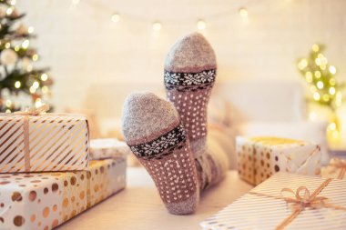 Noel ağacının yanındaki koltukta oturan kadın. Dişi bacaklar, kışın yün çoraplar, masaya koymak ve el yapımı hediye kutuları paketledikten sonra dinlenmek. Aile için hediyeler.