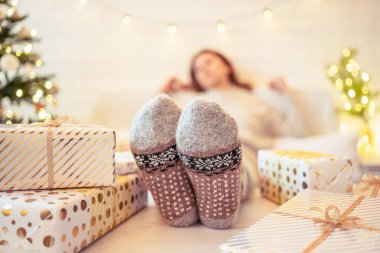 Noel ağacının yanındaki koltukta oturan kadın. Dişi bacaklar, kışın yün çoraplar, masaya koymak ve el yapımı hediye kutuları paketledikten sonra dinlenmek. Aile için hediyeler.