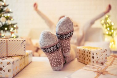 Noel ağacının yanındaki koltukta oturan kadın. Dişi bacaklar, kışın yün çoraplar, masaya koymak ve el yapımı hediye kutuları paketledikten sonra dinlenmek. Aile için hediyeler.