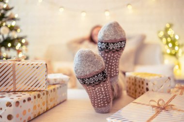 Noel ağacının yanındaki koltukta oturan kadın. Dişi bacaklar, kışın yün çoraplar, masaya koymak ve el yapımı hediye kutuları paketledikten sonra dinlenmek. Aile için hediyeler.