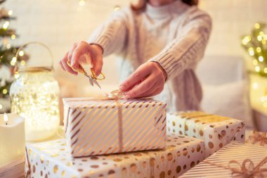 Noel ağacının yanındaki koltukta oturan ve el yapımı hediye kutularını masaya koyan kadın. Aile için hediyeler.