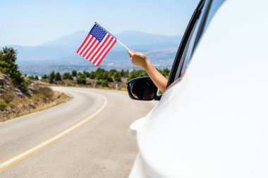 Kadın, açık arabanın camından Amerikan bayrağını tutuyor dağlarda serpentin yol boyunca sürüyor. Kavram