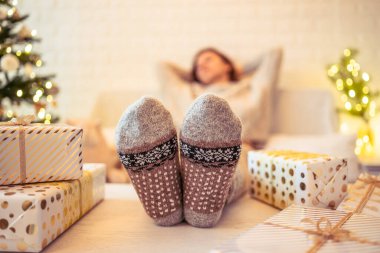 Noel ağacının yanındaki koltukta oturan kadın. Dişi bacaklar, kışın yün çoraplar, masaya koymak ve el yapımı hediye kutuları paketledikten sonra dinlenmek. Aile için hediyeler.