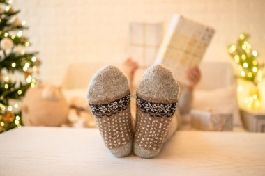 Noel ağacının yanındaki koltukta oturan kadın. Dişi bacaklar, kışın yün çoraplar, masaya koymak ve el yapımı hediye kutuları paketledikten sonra dinlenmek. Aile için hediyeler.