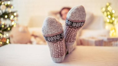 Noel ağacının yanındaki koltukta oturan kadın. Dişi bacaklar, kışın yün çoraplar, masaya koymak ve el yapımı hediye kutuları paketledikten sonra dinlenmek. Aile için hediyeler.