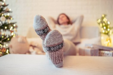 Noel ağacının yanındaki koltukta oturan kadın. Dişi bacaklar, kışın yün çoraplar, masaya koymak ve el yapımı hediye kutuları paketledikten sonra dinlenmek. Aile için hediyeler.