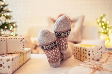 Noel ağacının yanındaki koltukta oturan kadın. Dişi bacaklar, kışın yün çoraplar, masaya koymak ve el yapımı hediye kutuları paketledikten sonra dinlenmek. Aile için hediyeler.