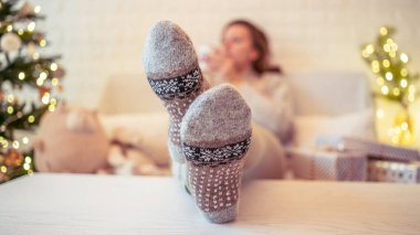 Noel ağacının yanındaki koltukta oturan kadın. Dişi bacaklar, kışın yün çoraplar, masaya koymak ve el yapımı hediye kutuları paketledikten sonra dinlenmek. Aile için hediyeler.