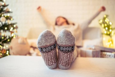 Noel ağacının yanındaki koltukta oturan kadın. Dişi bacaklar, kışın yün çoraplar, masaya koymak ve el yapımı hediye kutuları paketledikten sonra dinlenmek. Aile için hediyeler.